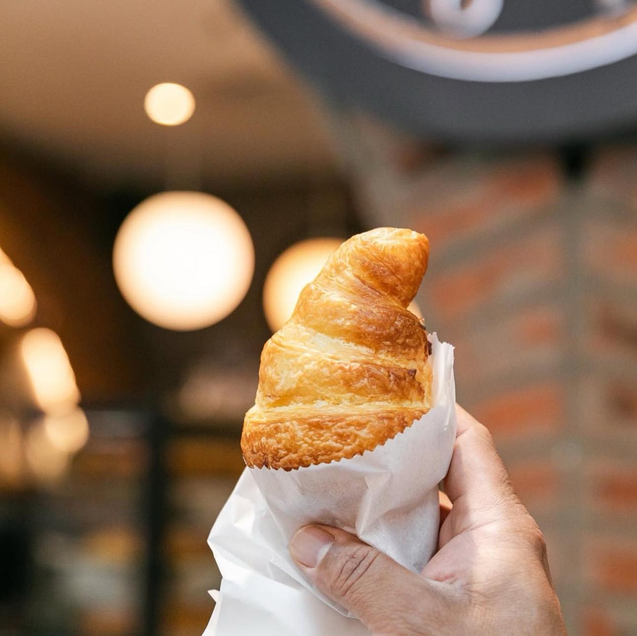 Hand-held classic French croissant in paper bag